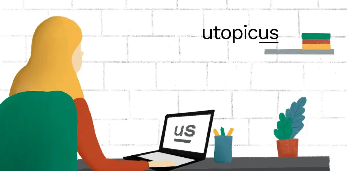 Una persona usa una laptop en un escritorio con lápices y una planta, frente a una pared de ladrillos blancos.
