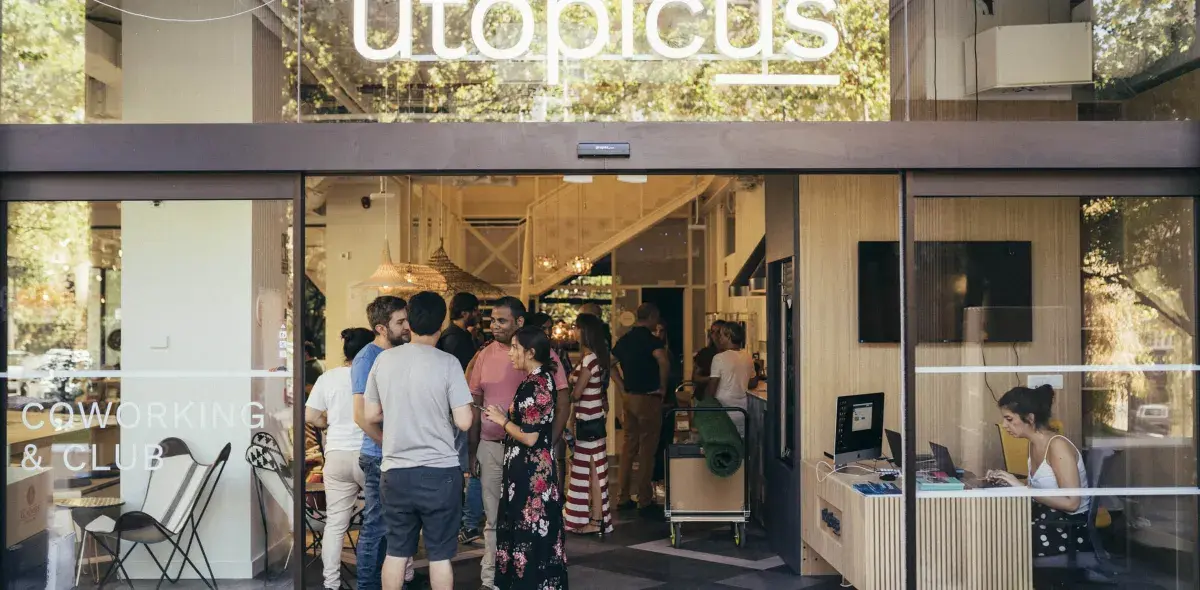 Personas conversando en un espacio de coworking llamado "utopicus". En el fondo, mesas y personas trabajando.