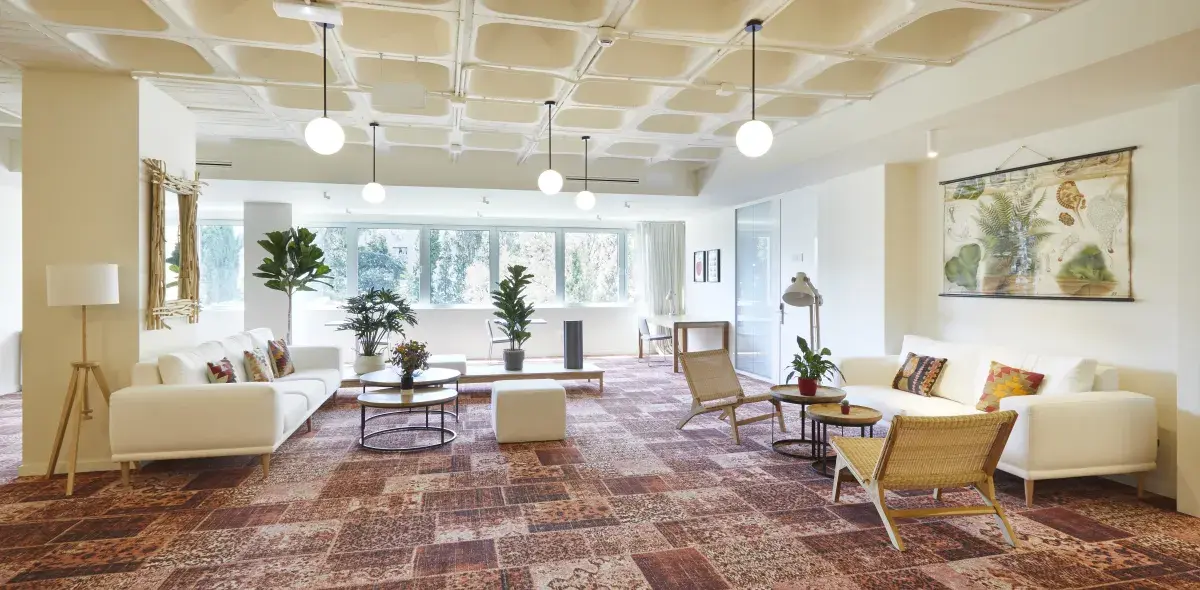 Sofás blancos organizados con mesas de centro y plantas, en una sala iluminada por grandes ventanales, con lámparas colgantes y paredes decoradas.
