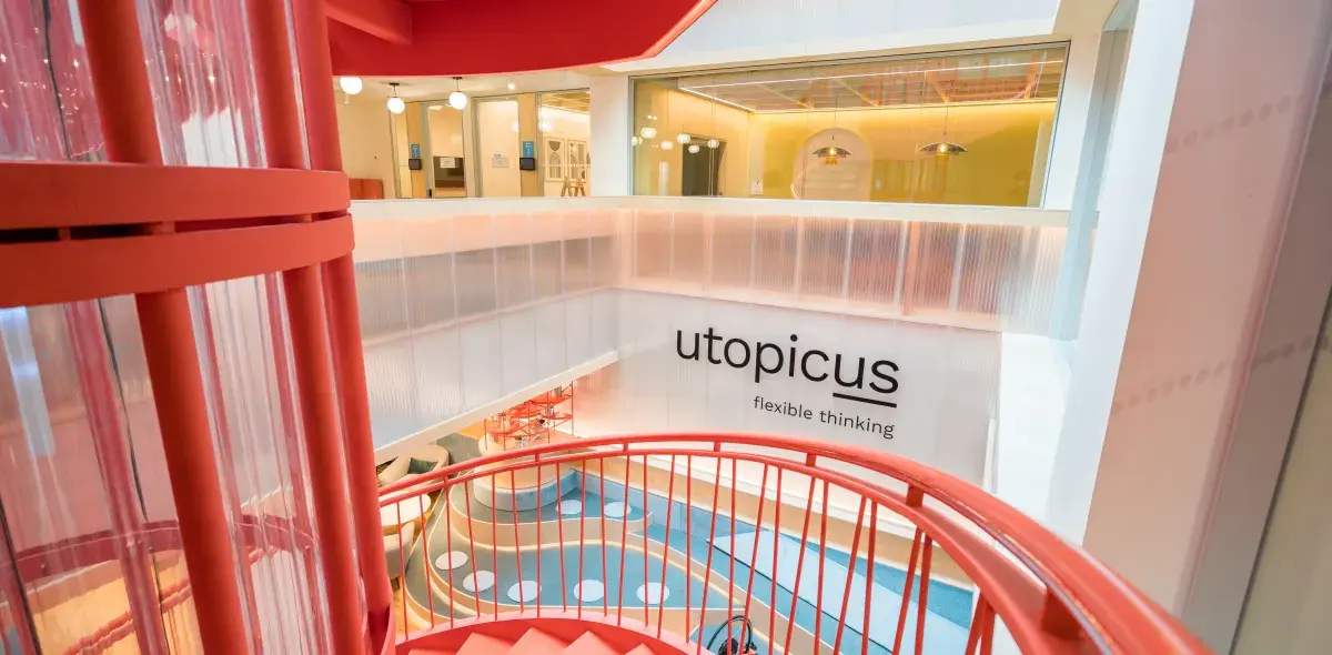 Una escalera roja de caracol desciende en un moderno espacio de oficina con paredes claras.