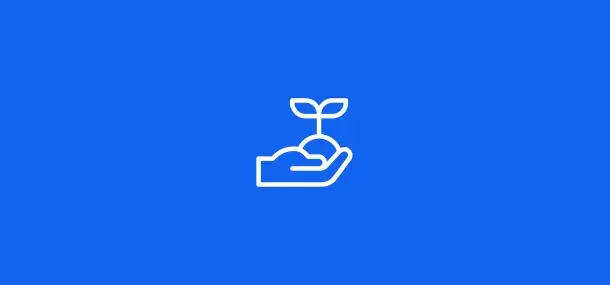 Una mano sostiene una pequeña planta con dos hojas, sobre un fondo azul simple.