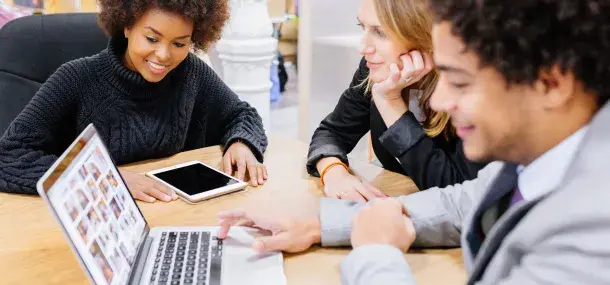 Personas trabajan colaborativamente alrededor de una mesa en una oficina, usando una computadora portátil y una tableta.