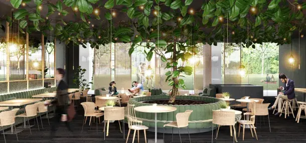 Un café moderno tiene mesas de madera y sillas, con un árbol central y luces colgantes. Grandes ventanales muestran un parque exterior, mientras personas conversan y caminan dentro del espacio.