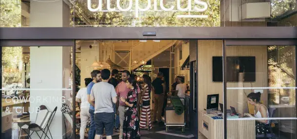 Personas conversando en un espacio de coworking llamado "utopicus". En el fondo, mesas y personas trabajando.