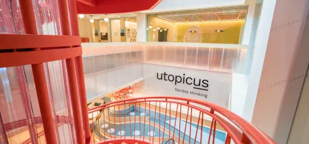 Una escalera roja de caracol desciende en un moderno espacio de oficina con paredes claras.