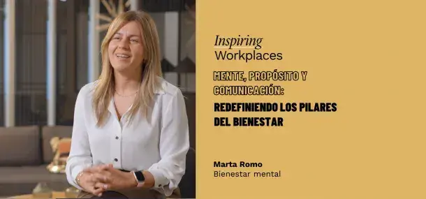 Una mujer sonríe, sentada en un ambiente de oficina moderna.